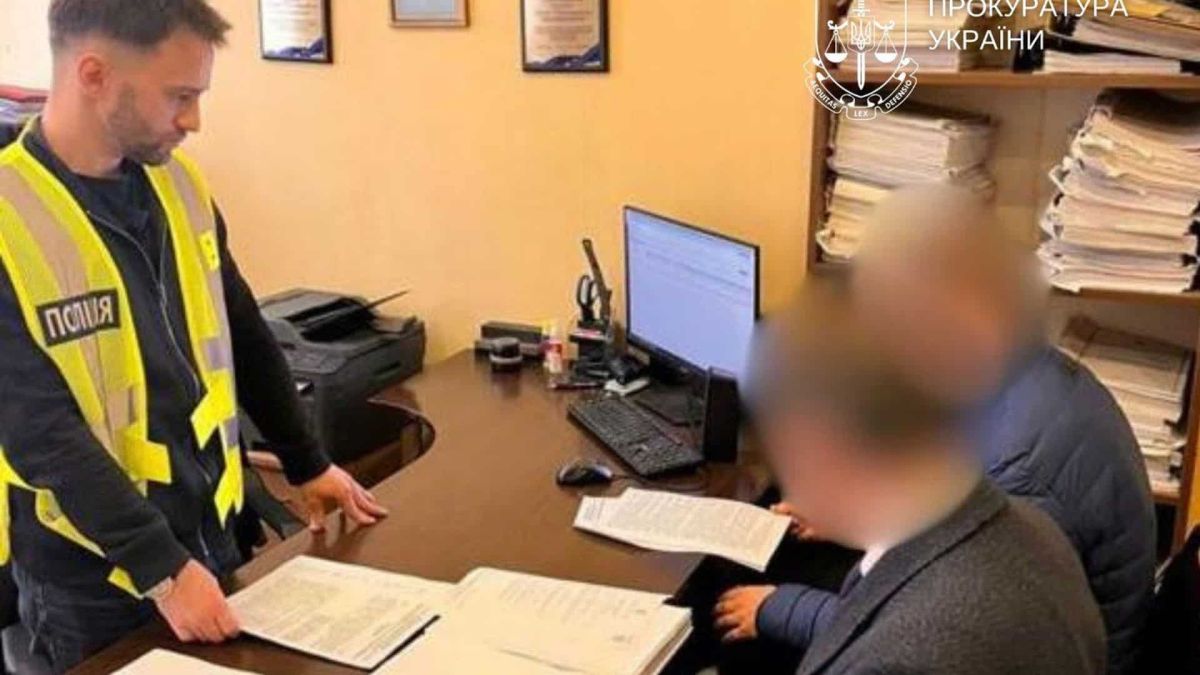 У Києві посадовцю КМДА повідомили про підозру через переплату 4,8 млн за генератори Поліцейський у жилеті стоїть біля столу, за яким сидить чоловік з розмитим обличчям