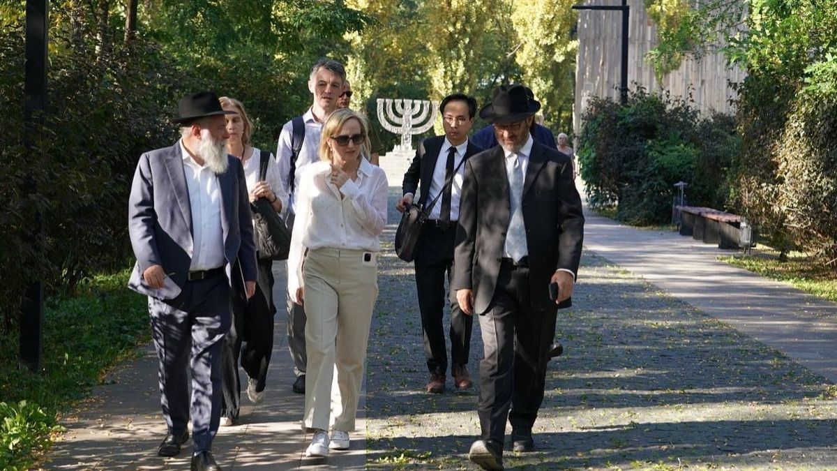 Нова повірена США Джулі Девіс розпочала каденцію з візиту до Бабиного Яру Група людей йде алеєю в парку, на задньому плані видно пам’ятний знак у вигляді менори