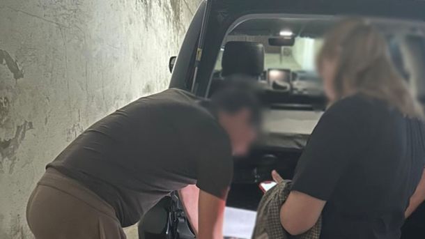 У Києві знайшли підпільний цех із 50 тоннами спирту Особа з розмитим обличчям підписує документи біля автомобіля під час слідчих дій у справі про земельну аферу у Голосіївському районі