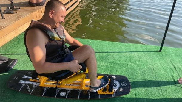 У Києві ветеранів запрошують на терапію з кіньми: верхова їзда та спілкування як частина реабілітації Чоловік у рятувальному жилеті сидить на спеціальному вейкборді з кріслом біля води