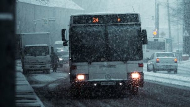 У Києві 289 одиниць спецтехніки «Київавтодору» прибирають вулиці від снігу Міський автобус Mercedes їде по засніженій дорозі під час снігопаду, увімкнені фари, на задньому плані інші автомобілі