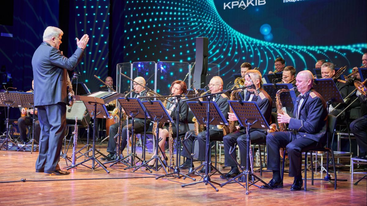 День джазу на Русанівці: президентський оркестр зіграє програму Whiplash 30 квітня Диригент керує президентським оркестром на сцені під час джазового концерту з написом Краків на екрані