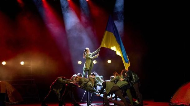 Київська поліція повернула жінці смартфон за 62 тис. грн, вкрадений біля ВДНГ На сцені театральної постановки група артистів у військових костюмах виконує композицію під драматичним червоно-чорним освітленням