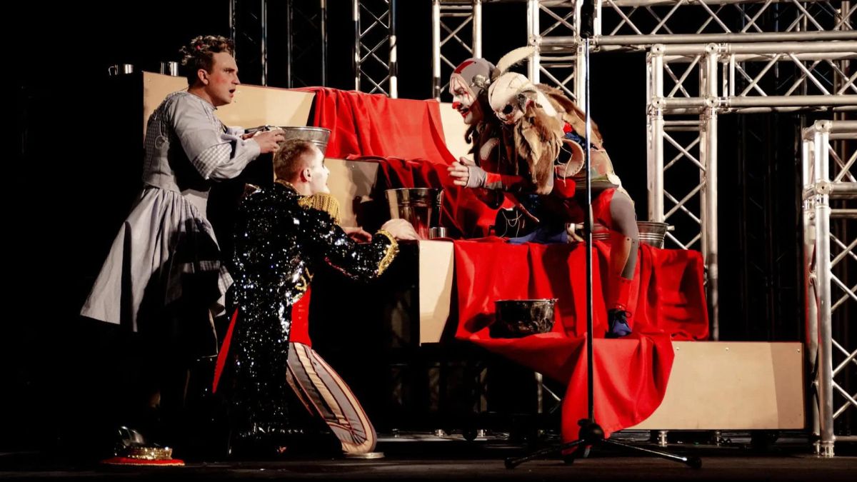 Сумський театр Щепкіна привезе до Києва «Алісу в Дивокраї» з чоловіками у всіх ролях Три актори в яскравих костюмах на сцені біля декорацій, вкритих червоною тканиною