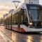 Головні новини Києва | Kyiv.News Ілюстративне фото: трамвай їде міською вулицею на тлі осіннього заходу сонця, перехожі на тротуарі