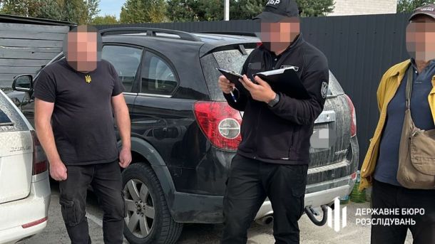 Два марші в центрі Києва 21 червня: КиївПрайд і Хода на захист сім’ї Троє чоловіків стоять біля чорного автомобіля на парковці, один у чорній формі з написом "ДБР" веде записи в блокноті, інші двоє у цивільному одязі