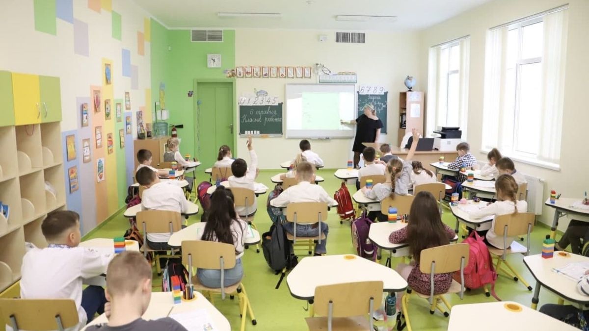 Київщина повертається до навчання: освітня омбудсманка закликає не примушувати педагогів працювати в холодних школах Клас із учнями за партами, які слухають учительку біля дошки з проєктором