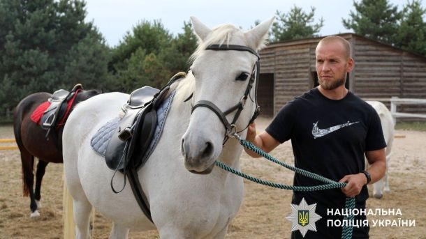 Київщина: поліцейські ветерани проходять іпотерапію для відновлення після поранень Чоловік у чорній футболці тримає за повід білого коня із сідлом