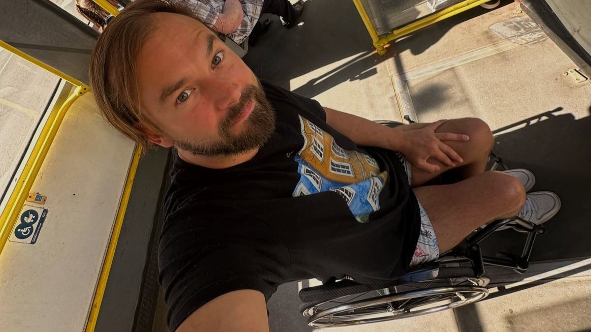 «У Києві транспорту майже нема». Дмитро Щебетюк розповів про досвід поїздки у колісному кріслі зображення чоловіка у візку на відкритому повітрі, світле сонячне світло, повсякденний стиль, позитивна атмосфера, знімок у києві, сучасне міське життя, міська інфраструктура, безбарвний фон, сонячні тіні, активний спосіб життя.