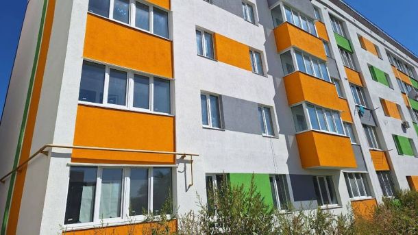 У Макарові завершують капремонт п’ятиповерхівки, пошкодженої під час боїв у 2022 році Київський житловий будинок з яскраво пофарбованими фасадами в зеленому, сірому та оранжевому кольорах на сонячному день.