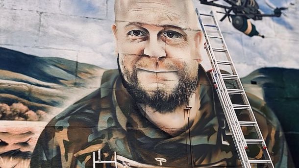 ТРЦ Retroville скасовує безплатне паркування: мешканці «Варшавського» обурені Портрет героя на стіні будинку, біля стіни стоїть драбина