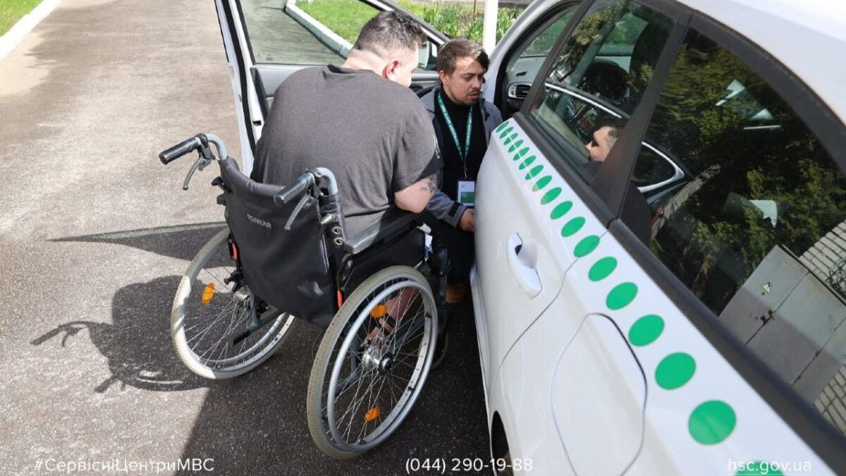 Кабмін підвищив штрафи за паркування на місцях для людей з інвалідністю Ветеран з інвалідністю у кріслі колісному поруч з автомобілем Сервісного центру МВС, поряд консультант