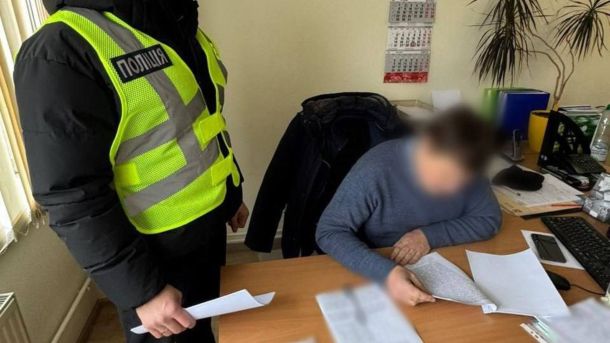 У Києві судитимуть жінку за погрозу підірвати управління поліції Поліцейський у сигнальному жилеті вручає документи підозрюваному посадовцю в офісі, обличчя підозрюваного розмите