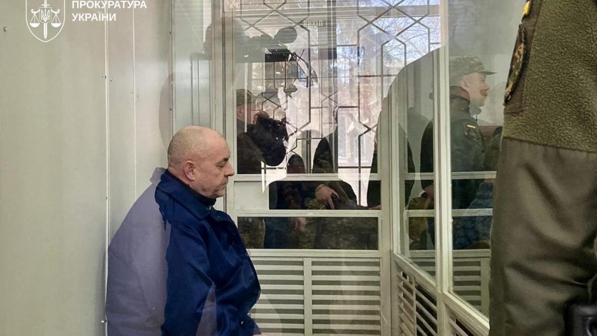 Довічне ув'язнення за розстріл полонених ЗСУ на Курщині Засуджений російський військовий у синій куртці сидить за склом у залі Шевченківського районного суду Києва, поруч конвоїр у формі
