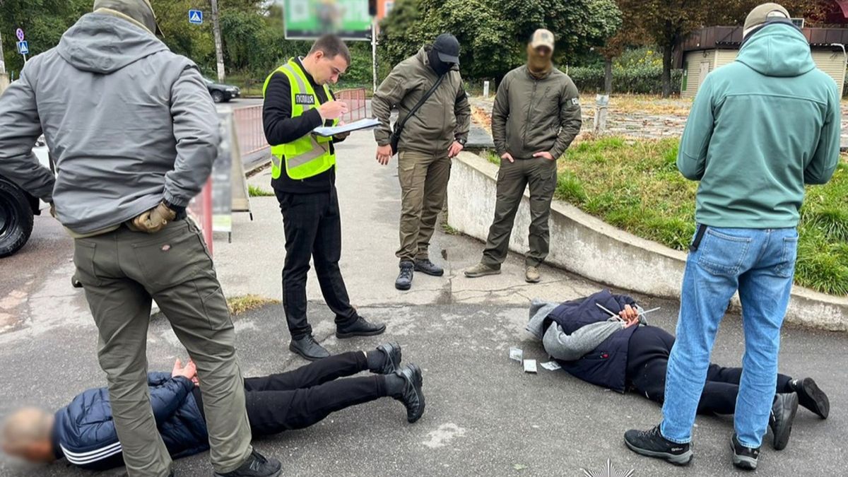 Поліція і СБУ викрили схеми «ухилення»: фіктивні роботи, довідки, виїзд за кордон Пʼятеро чоловіків стоять на вулиці, біля них двоє чоловіків лежать на асфальті з руками за спиною. Один з тих, хто стоїть – у поліцейській формі.