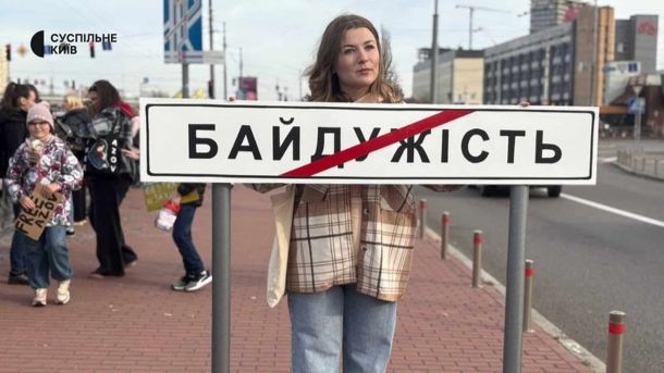 Біля станції метро «Героїв Дніпра» демонтували незаконні кіоски Жінка тримає дорожній знак з написом "БАЙДУЖІСТЬ", перекреслений червоною смугою