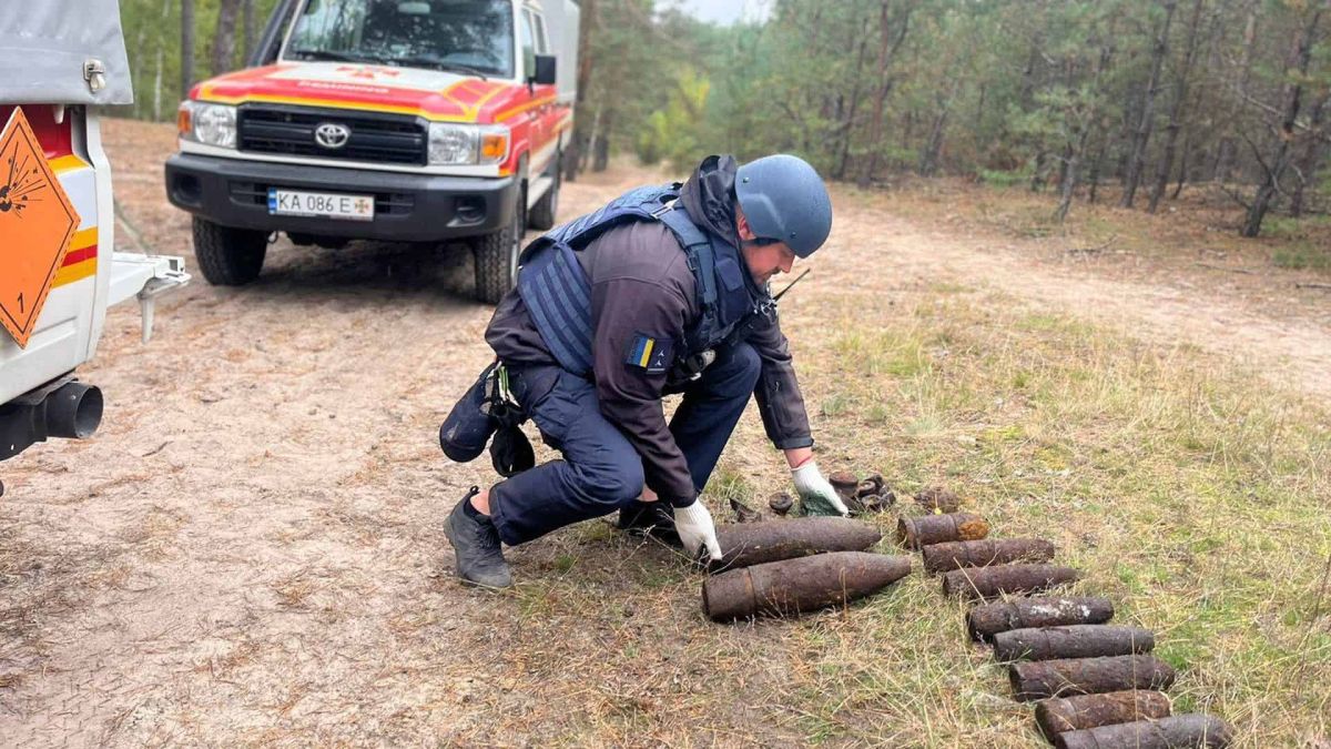 Деснянський район: рятувальники знешкодили боєприпаси часів Другої світової війни Сапер у захисному шоломі й бронежилеті обережно розкладає на землі знайдені артилерійські снаряди в лісі