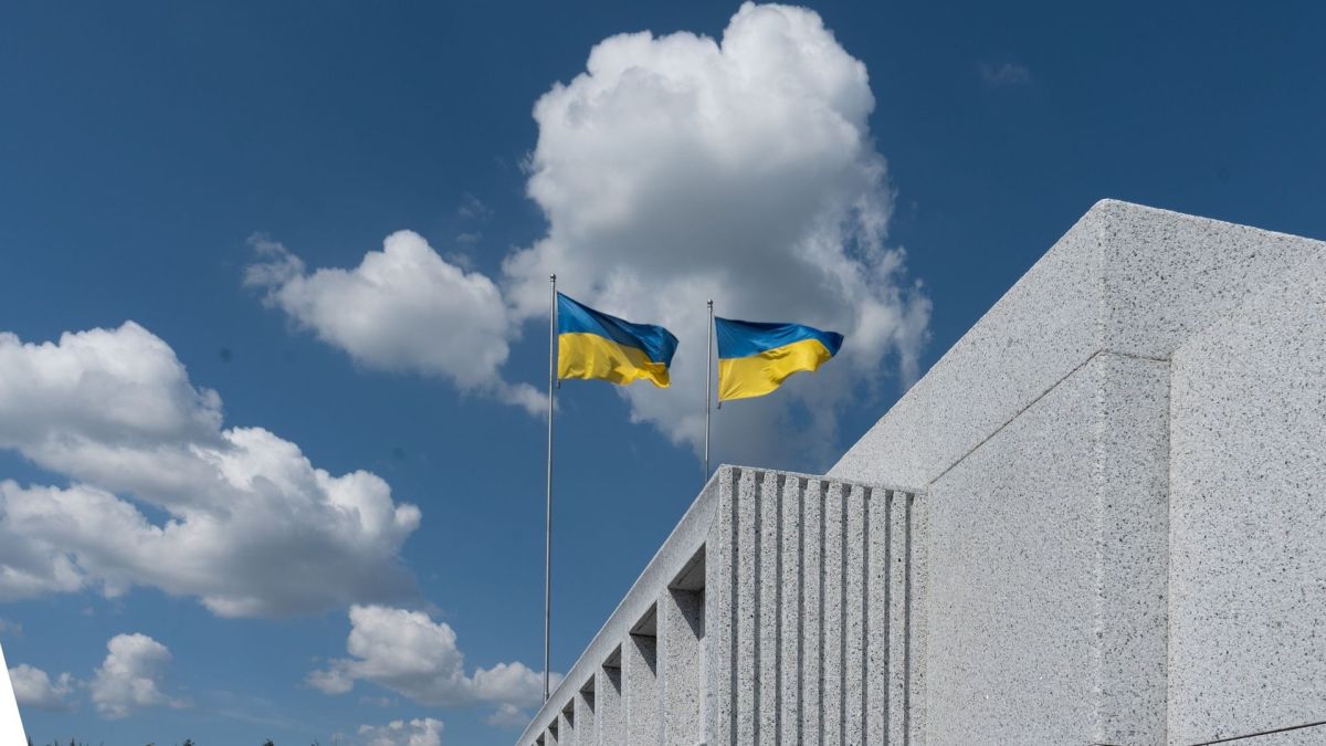Суд підтвердив законність будівництва Національного військового меморіального кладовища Два українські прапори майорять на флагштоках над сучасною білою будівлею на тлі синього неба з хмарами