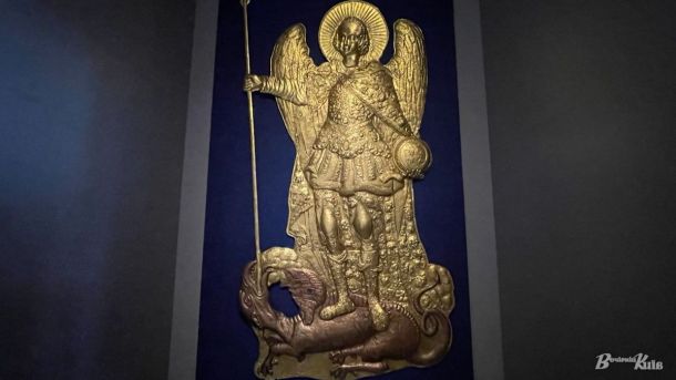 Виставка про Архистратига Михаїла у Києві: барельєф XVIII століття та артефакти УНР Золота гравюра з образом святого Михайла, що бореться зі злом, у темній залі. Висока якість, детальний дизайн, історична цінність, мистецький шедевр, музейна експозиція, культурна спадщина України.