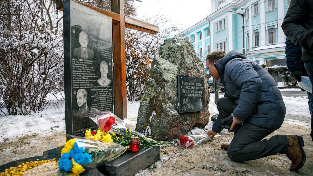 У Маріїнському парку вшанували загиблих 18 лютого 2014 року Чоловік схиляється на коліно біля меморіальної дошки загиблих Небесної Сотні з квітами та свічками взимку