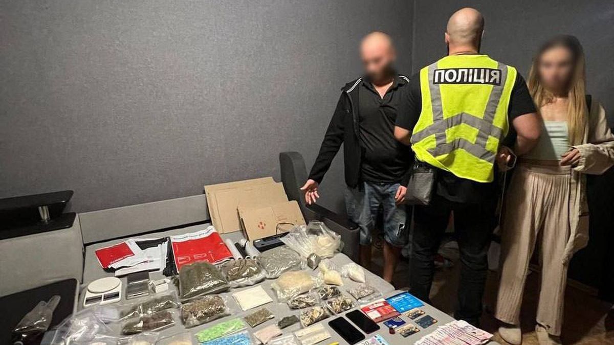 У Києві затримали наркоугруповання та вилучили наркотиків на 4 млн грн Поліцейський у жилеті поруч із затриманим чоловіком і жінкою, поруч вилучені наркотики, гроші та банківські картки