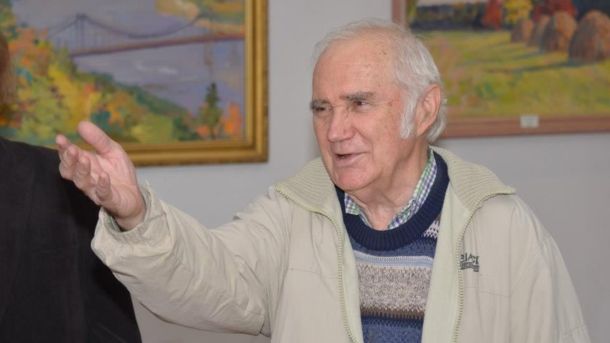 Помер Олег Животков — київський живописець і педагог Художник Олег Животков жестикулює рукою на фоні своїх пейзажних картин у галереї