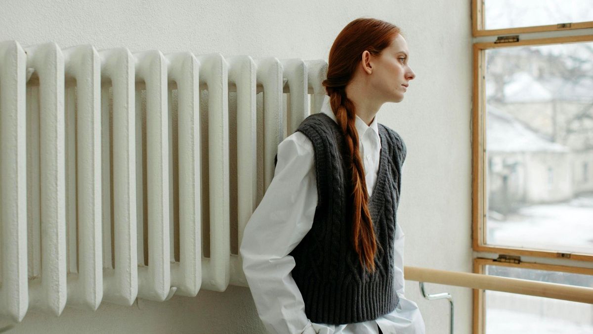 Опалення в Києві 2025–2026: від графіків до компенсацій Молода жінка в зимову пору гріється біля радіатора