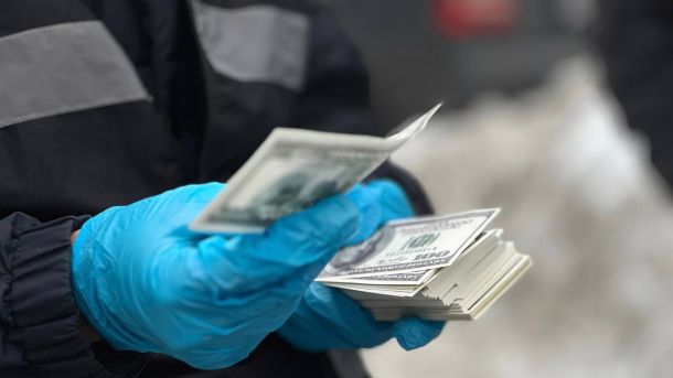 Хірурга в Києві підозрюють у пошкодженні лицьового нерва під час операції Правоохоронець у захисних рукавичках тримає стопку вилучених 100-доларових банкнот