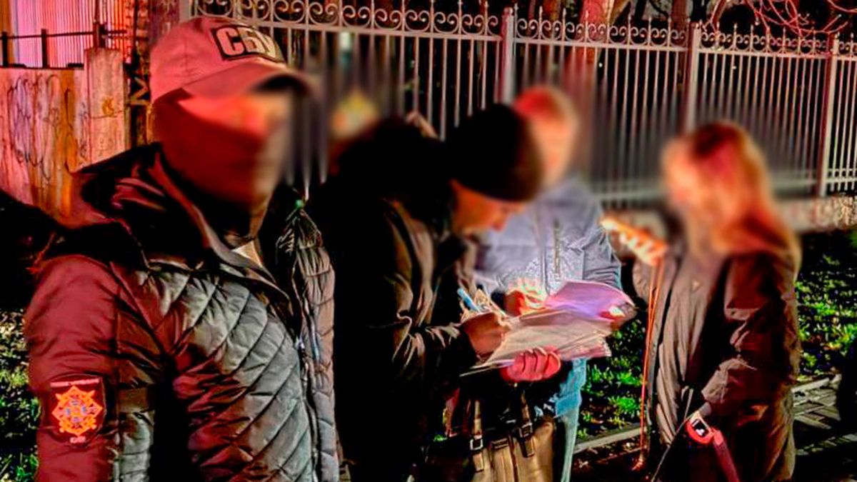 Фіктивні довідки про догляд за людиною з інвалідністю: у Києві викрили схему Правоохоронці стоять біля чоловіка і жінки, які підписують документи в темряві