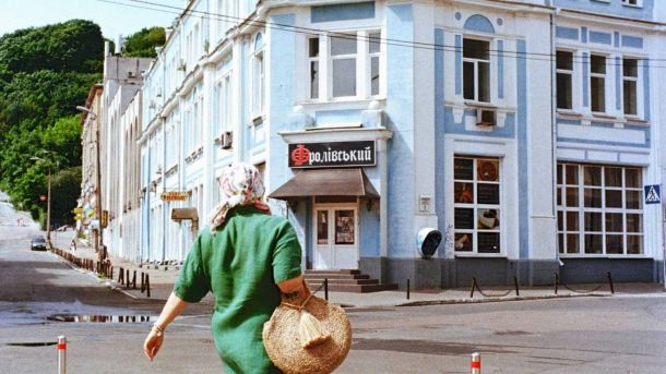 Двох киян хотіли переправити до Угорщини за $26 000: підозра Жінка у зеленій сукні йде по бруківці Фролівської вулиці на Подолі повз будівлю з написом «Фролівський» — квартал поблизу заарештованого Ткацького цеху на Фролівській, 4