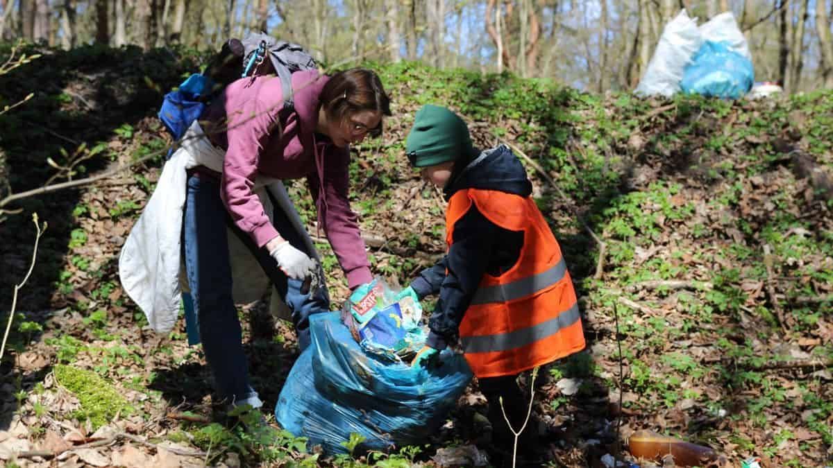 У Києві 20 вересня відбудеться Марш прибирання в Голосіївському парку Жінка та дитина у помаранчевому жилеті збирають сміття до синього мішка під час прибирання в лісі