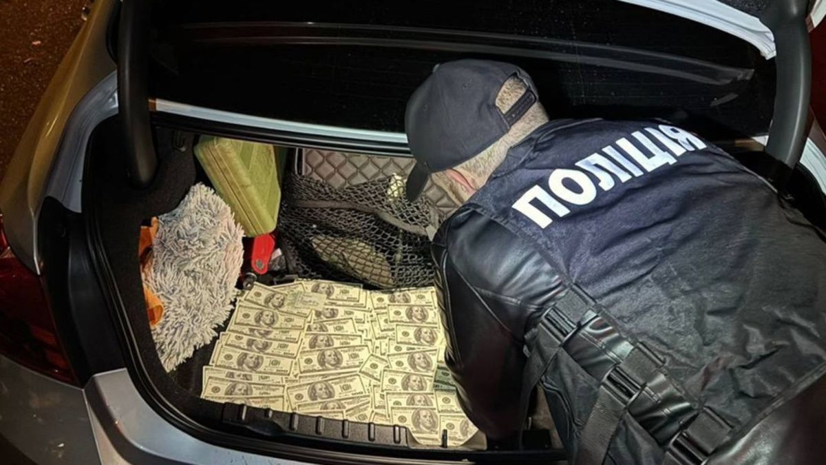 Вимагав $36 тис. за зняття з військового обліку: у Києві справу передали до суду Поліцейський оглядає вилучені долари в багажнику автомобіля під час затримання посадовця, який вимагав хабар за зняття з військового обліку
