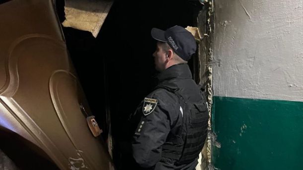 Нова масована атака РФ: знеструмлено 7 областей, запроваджені графіки обмежень Працівник поліції біля зруйнованих пожежею дверей квартири