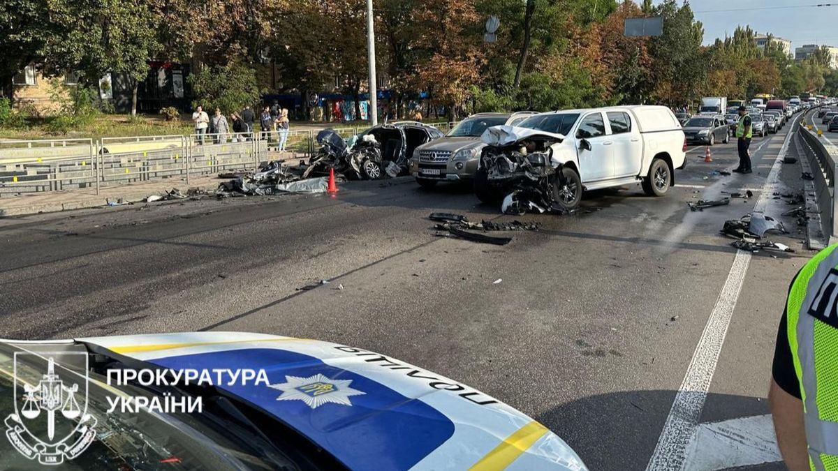ДБР розслідує смертельне ДТП у Києві за участі військового Pas accidentom на мосту у Києві, пошкоджені автомобілі та дорожні уламки, дорожня служба реагує, поліція організовує рух, фото відображає наслідки масштабної автокатастрофи.
