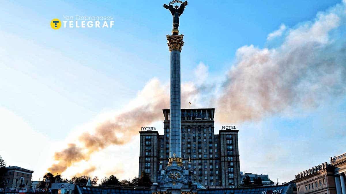 Атака дронами на Київ: уламки влучили в будівлю Кабміну Київський Майдан Незалежності з пам’ятником у центрі, з палаючим димом у небі на тлі будівель. У центрі зображена історична та сучасна частина столиці України.