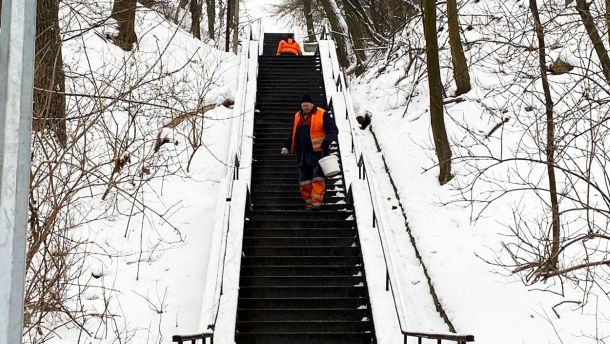 Перший день весни на Київщині: до +7° та ожеледиця Працівники комунальної служби в оранжевих жилетах очищають від снігу металеві сходи в парку