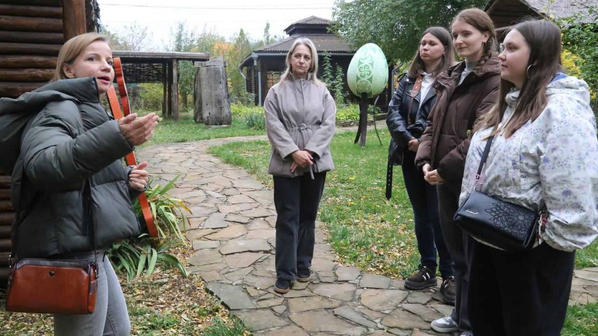 Вишгородський заповідник показав гостям гончарство і бортництво Київщини Екскурсоводка розповідає групі жінок на кам’яній доріжці Екоосередку у Вишгородському заповіднику, позаду дерев’яні будівлі й писанка