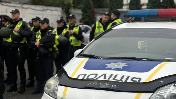 У Києві викрили організаторів схем із втечею за кордон та фіктивним бронюванням На передньому плані поліцейський автомобіль із увімкненим проблисковим маячком, на задньому — група поліцейських