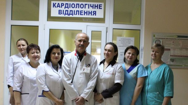 Кардіохірургічна допомога у Києві стала безплатною Семеро медичних працівників у білих та бірюзових халатах стоять перед дверима кардіологічного відділення лікарні