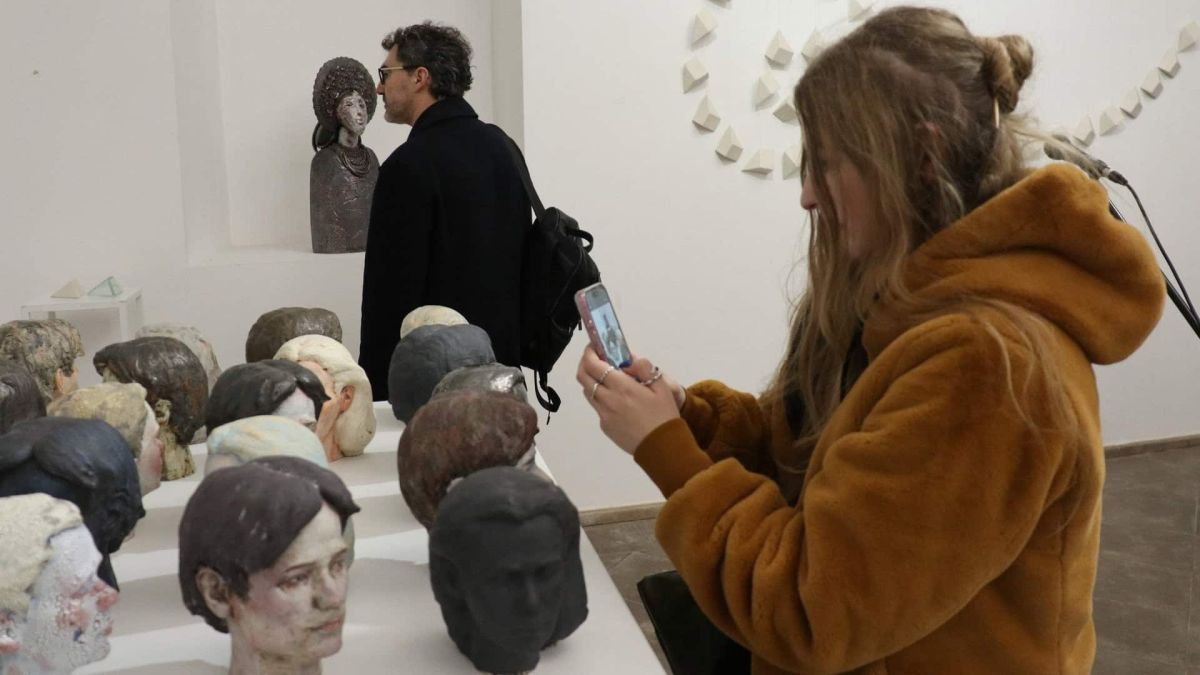 У Софії Київській відкрили фестиваль кераміки «Пам’ять глини» Дівчина з телефоном стоїть біля глиняних фігур і фотографує їх, фігури - це голови різних людей