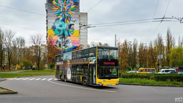 Київ запустив ще один двоповерховий автобус, але не без недоліків Двоповерховий жовто-чорний автобус проїжджає повз багатоповерхівку з яскравим муралом