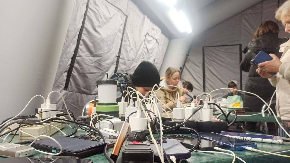 Жителі Славутича досі без світла: електрику повернули тільки в лікарню і школи Кілька людей сидять в пункті незламності, на передньому плані ризетки і зарядні пристрої