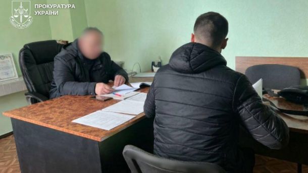 Переплата 670 тис. за парк «Орлятко»: посадовця «Київзеленбуду» судитимуть Двоє чоловіків сидять за столом в кабінеті під час допиту, обличчя одного з них розмите