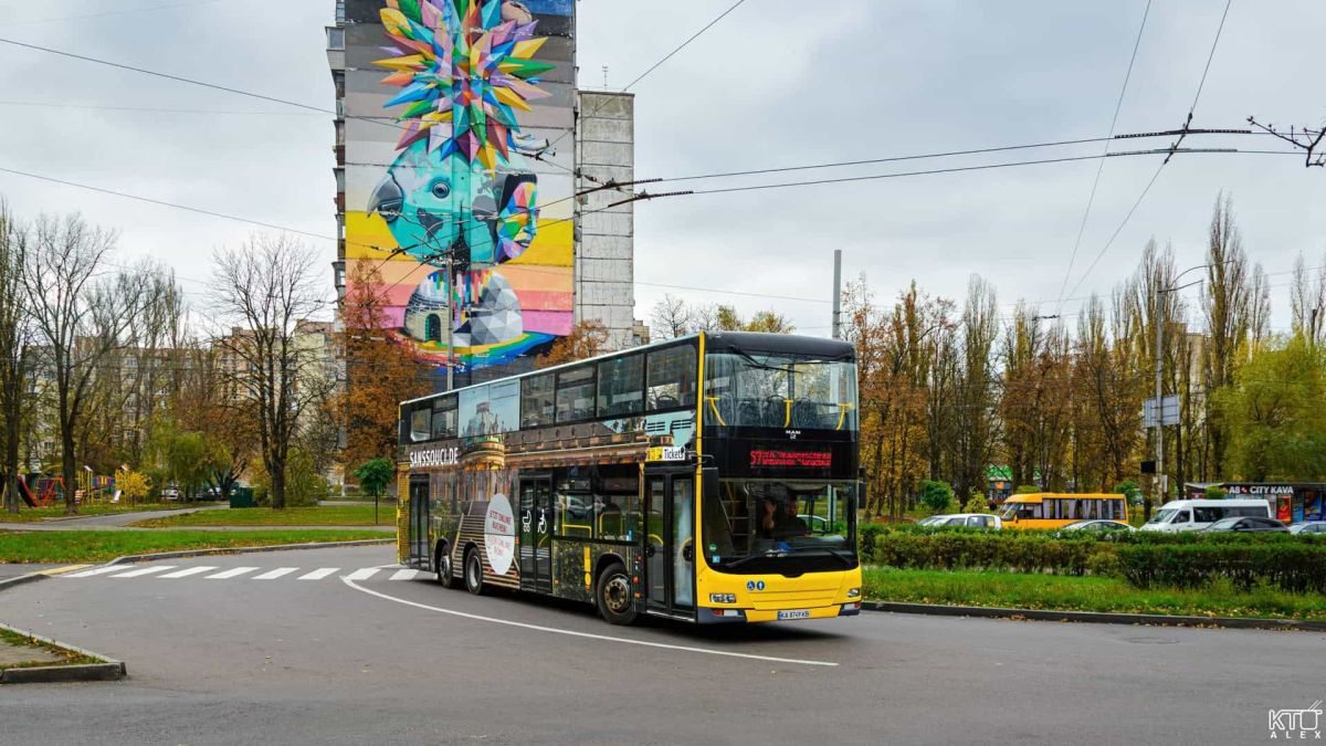 Київ запустив ще один двоповерховий автобус, але не без недоліків Двоповерховий жовто-чорний автобус проїжджає повз багатоповерхівку з яскравим муралом