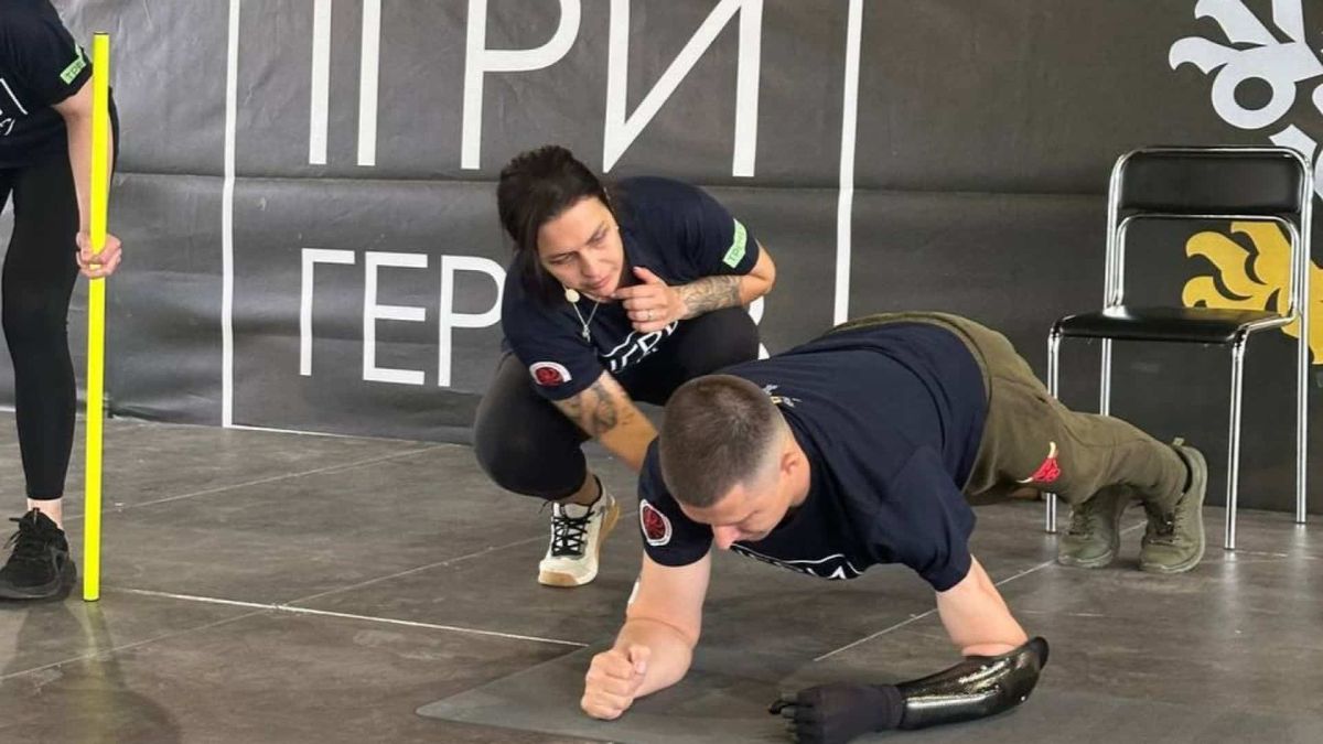 «Ігри Героїв» у Києві: ветерани з ампутаціями долучилися до відкритого тренування Військовий із протезом руки виконує вправу «планка», а інструкторка поруч підтримує його