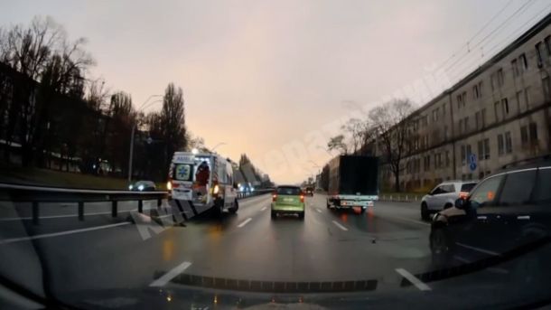 У Києві станції міської електрички заговорили голосами зірок та волонтерів Вид із машини на мокру дорогу, де видно "швидку" та інші автомобілі під час сутінок