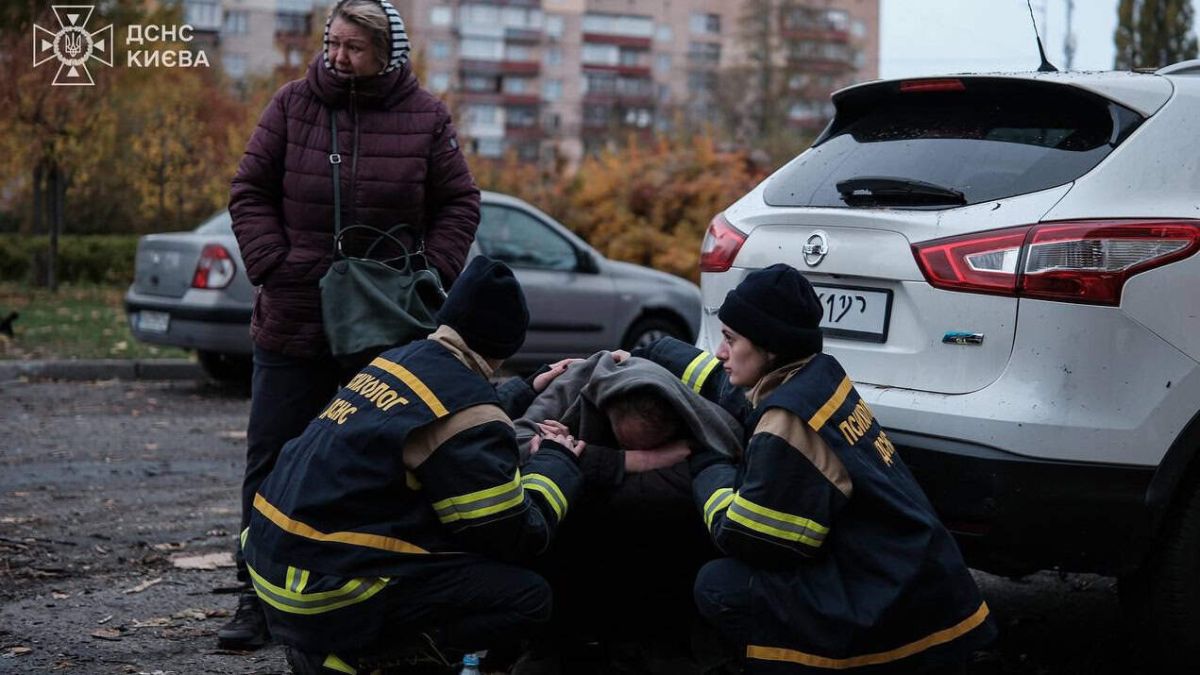 В столиці розгорнули штаби допомоги після нічної атаки дронів: адреси Працівники ДСНС сидять навколішки біля людини, яка теж навколішки сидить в ковдрі у дворі біля зруйнованого будинку