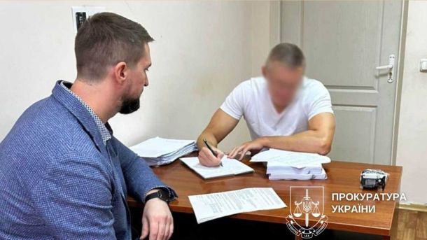 У Києві поліцейські затримали хулігана, який зламав світильник у метро — йому світить до 5 років Слідчі дії: двоє чоловіків сидять за столом у кабінеті. Один у білій футболці з розмитим обличчям заповнює документи