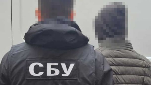 Світло без перерв: які райони Києва та області 26 жовтня не вимикатимуть Працівник із надписом на куртці ззаду «СБУ» стоїть біля чоловіка в капюшоні, ймовірно це підозрюваний