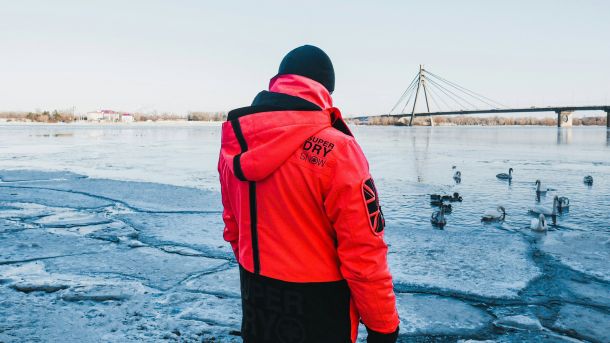 Київщина 18 лютого: сніг вдень і мороз до -17° Людина на березі Дніпра дивиться на крижини та битий лід, на тлі мосту та качок на воді